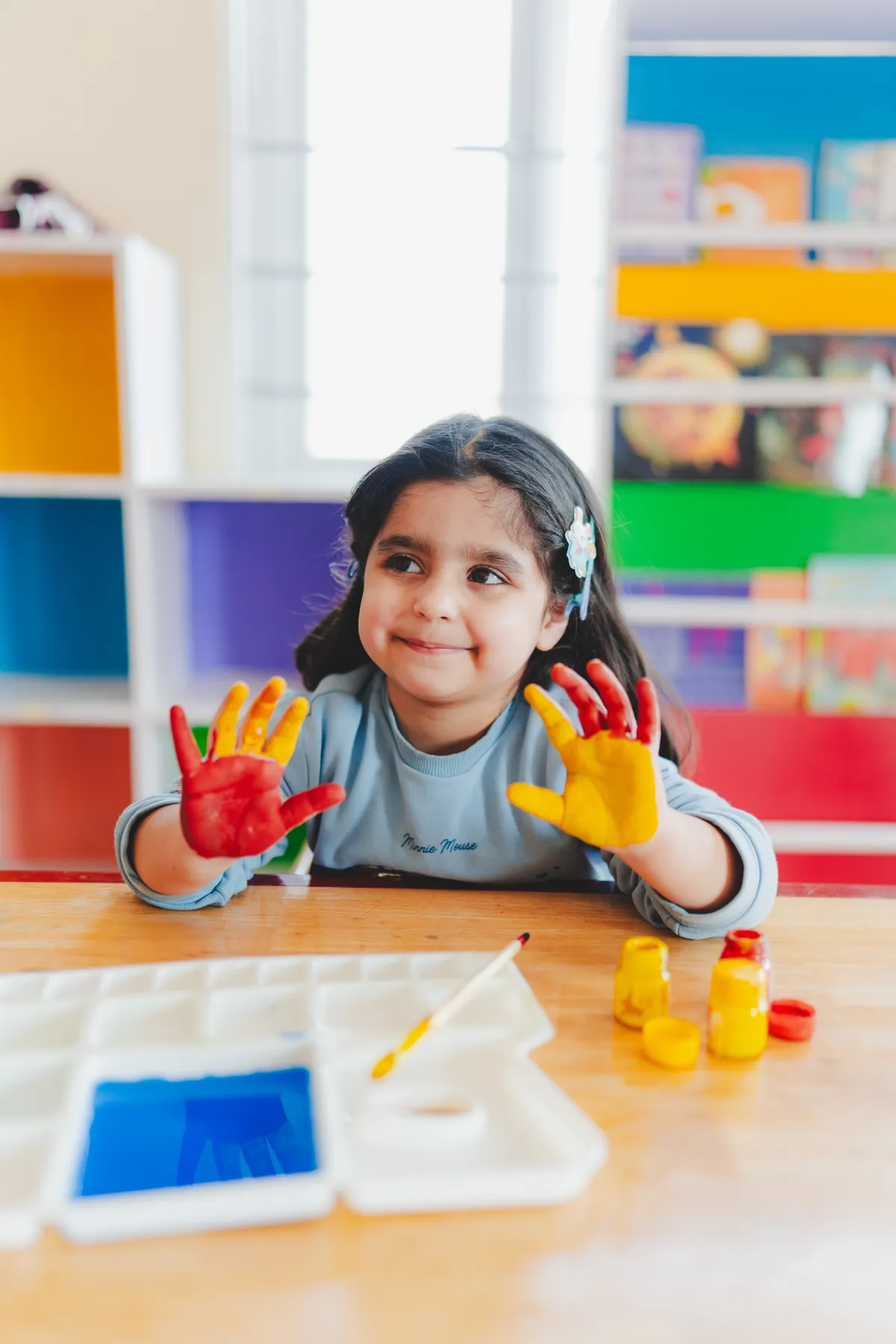 A happy child showing off her red and yellow painted hands