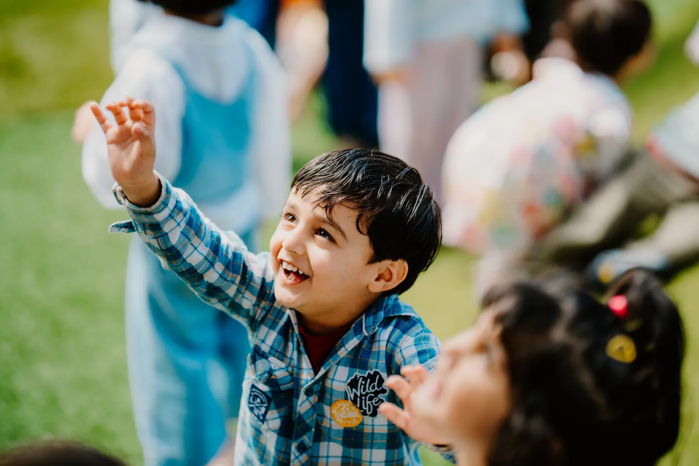 A joyful boy reaching up and laughing during outdoor play