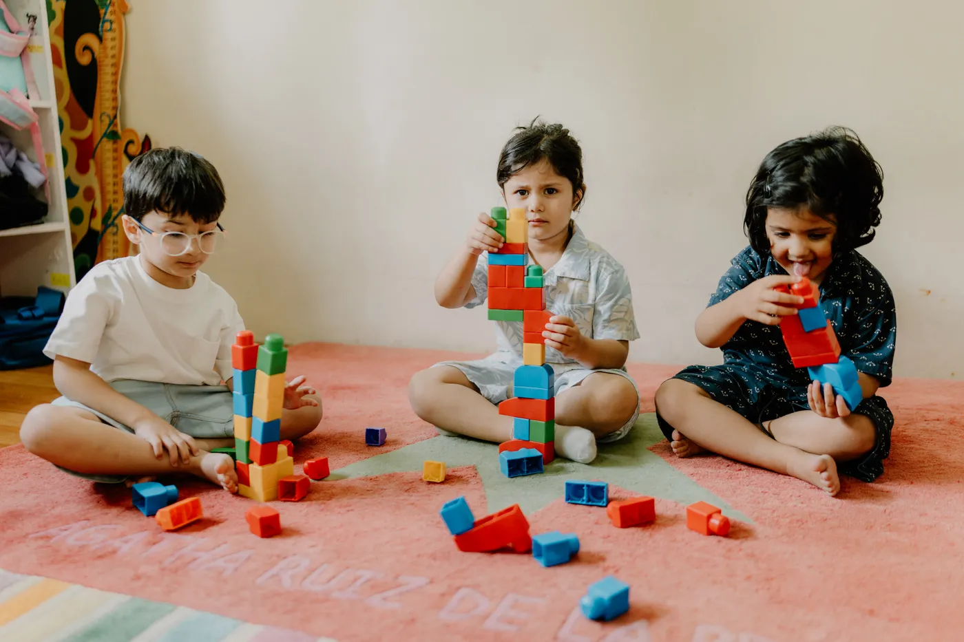 Three children stacking colourful blocks into towers