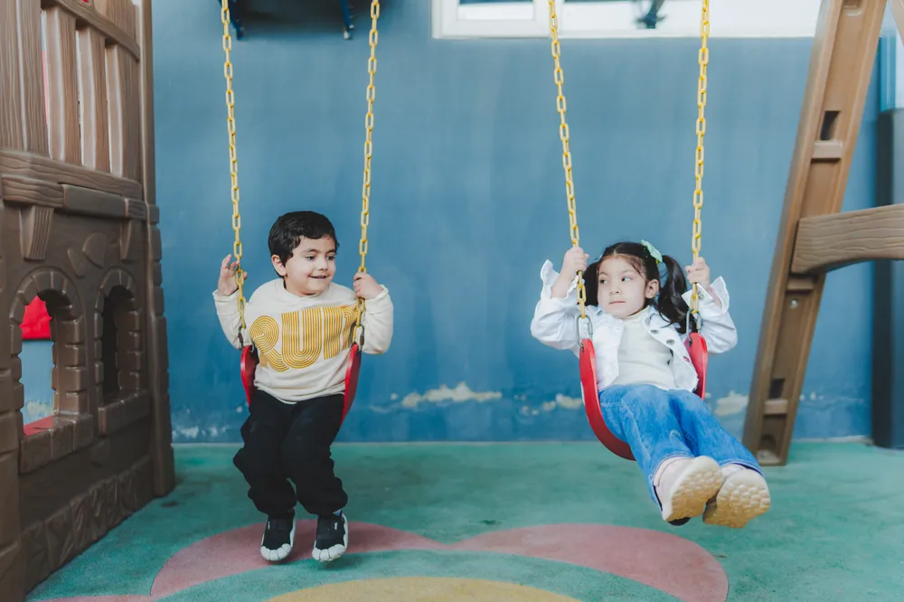 Two children enjoying the swings in the soft play area