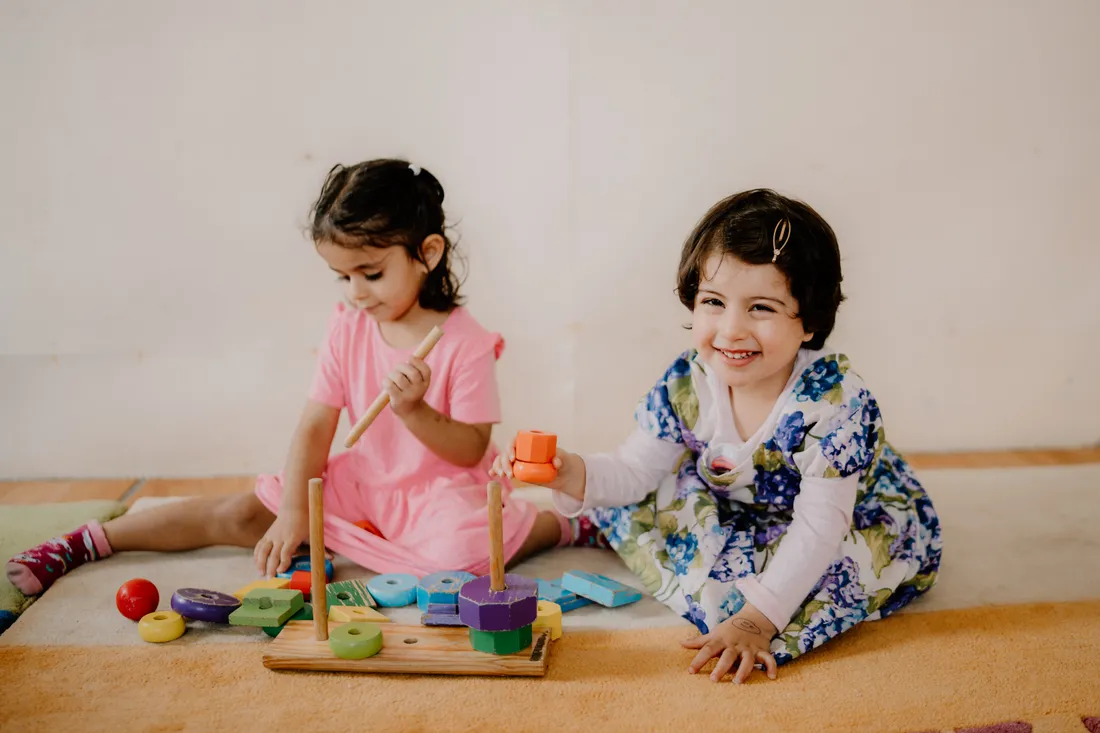 Two children developing fine motor skills with a wooden stacking toy